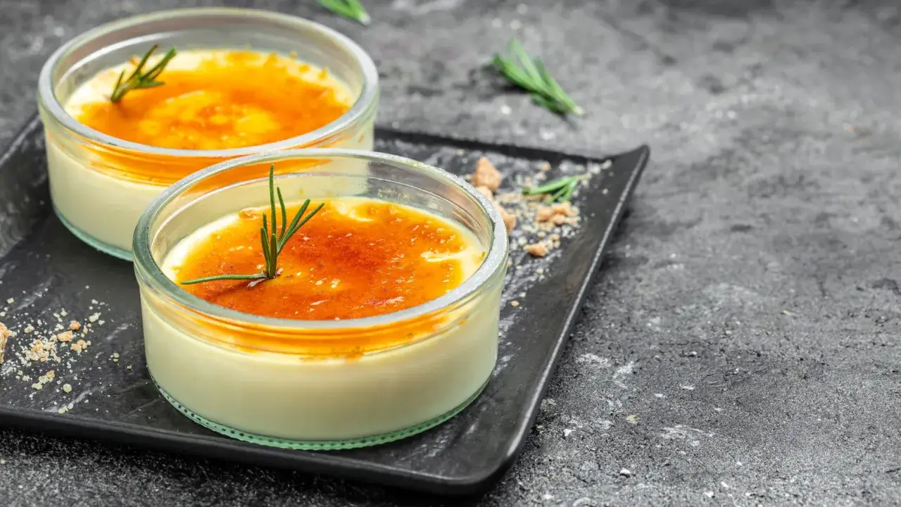 Två krämiga creme brulee i glasformar, toppade med karamelliserat socker och en rosmarinkvist. Perfekt dryck till creme brulee.