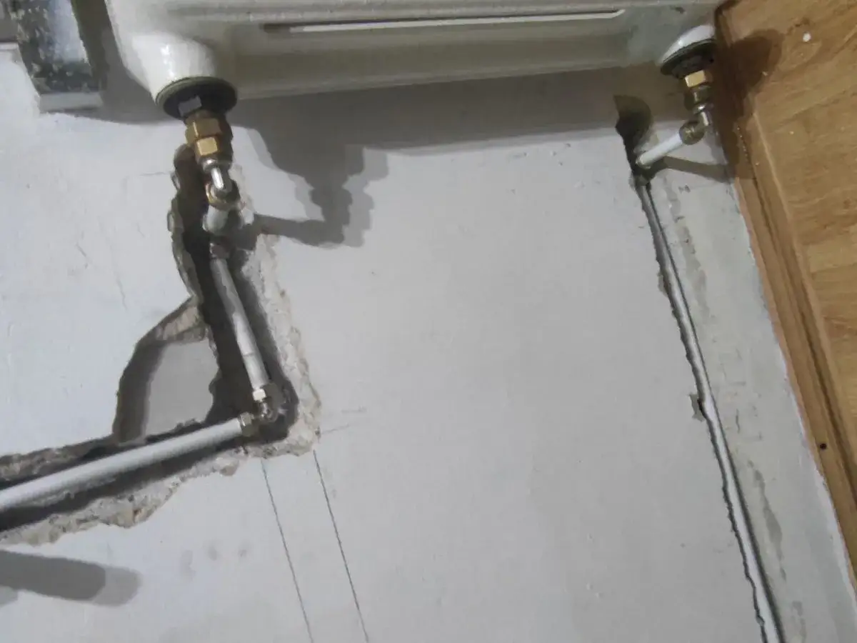 Instalacja hydrauliczna grzejnika łazienkowego do starej instalacji. Widoczne rury i złączki mosiężne.