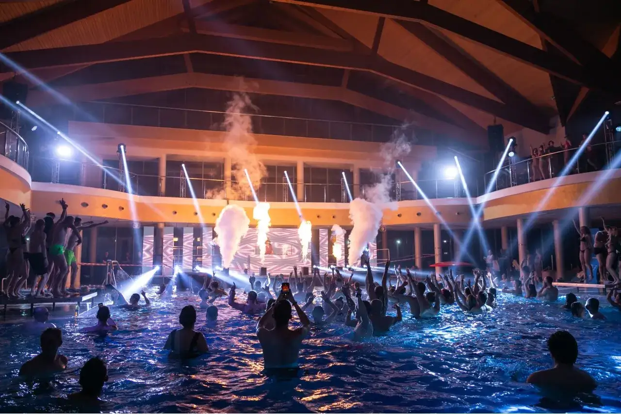 Noc basenów w Bukowinie: tłum ludzi w wodzie, efekty pirotechniczne, światła i DJ na scenie.