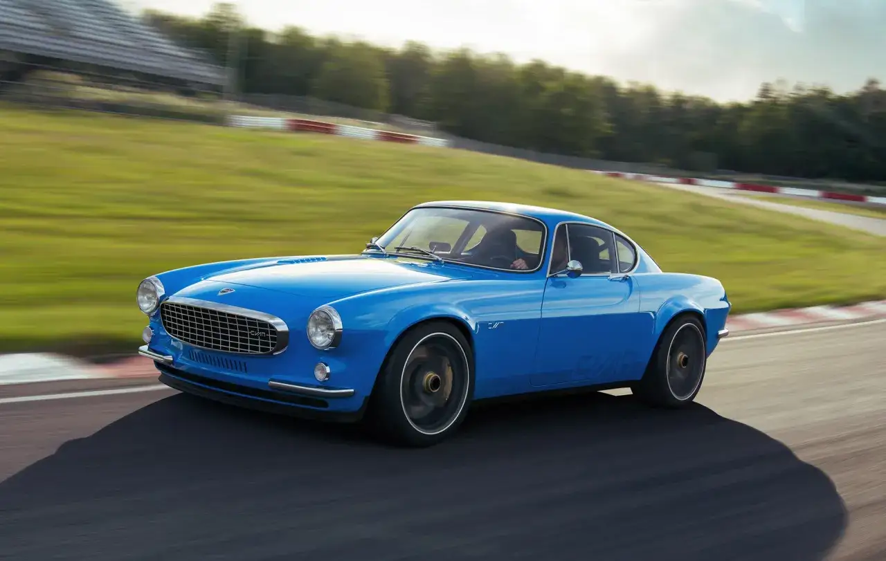 En blå cyan P1800 kör fort på en bana, med grönskande kullar och läktare i bakgrunden.