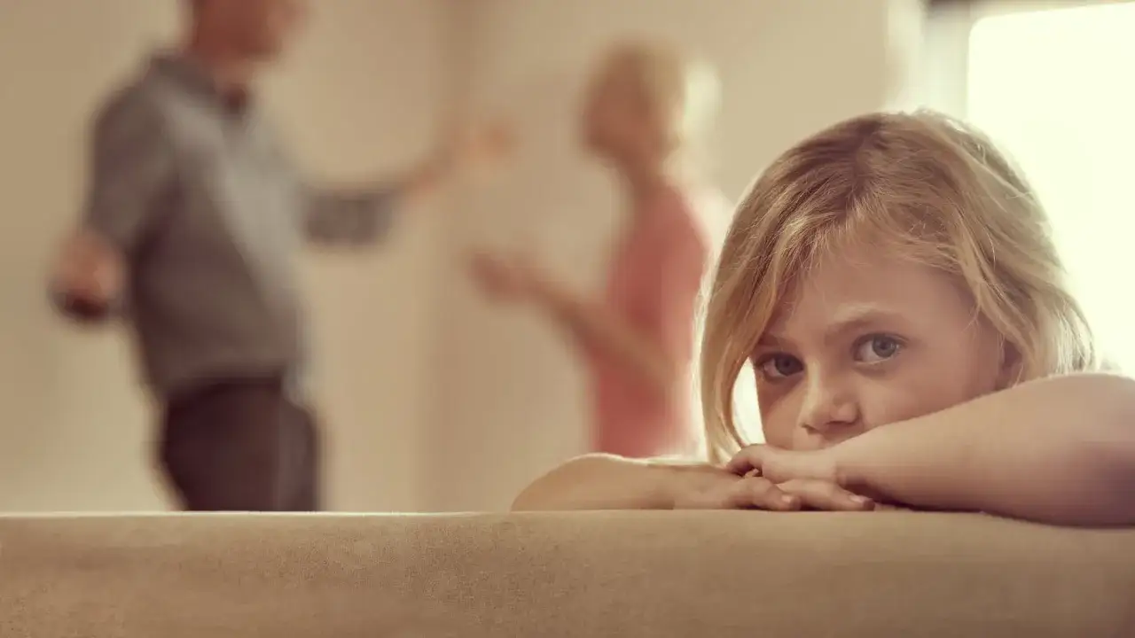 Ni&ntilde;a rubia con mirada triste, oculta tras un sof&aacute;. Al fondo, sus padres discuten. Siente que mi hijo cada vez se porta peor.