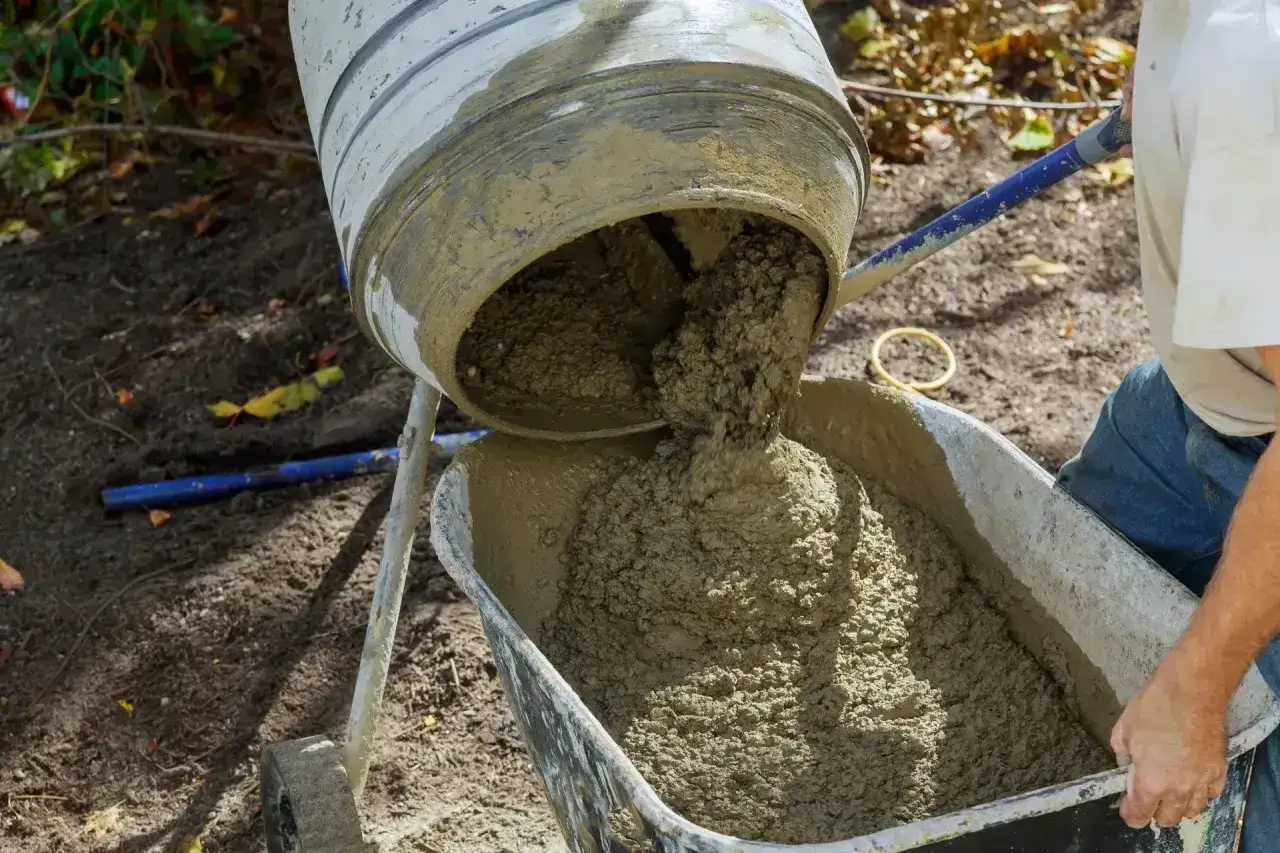 Betoniarka 150l wylewa świeży beton do taczki. Właściwa ilość cementu jest kluczowa dla trwałości konstrukcji.