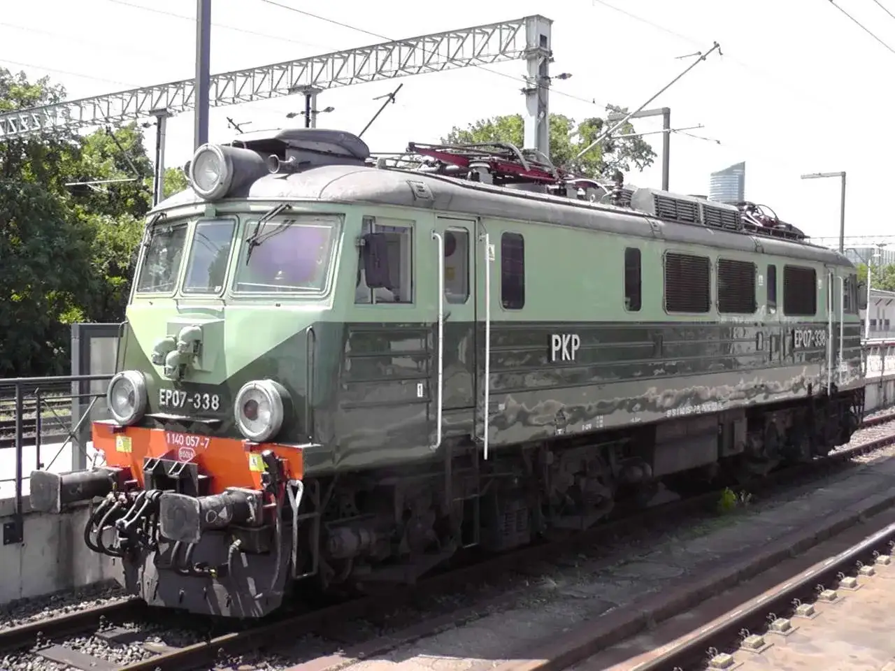 Zielona lokomotywa PKP EU07-338 stoi na torach.