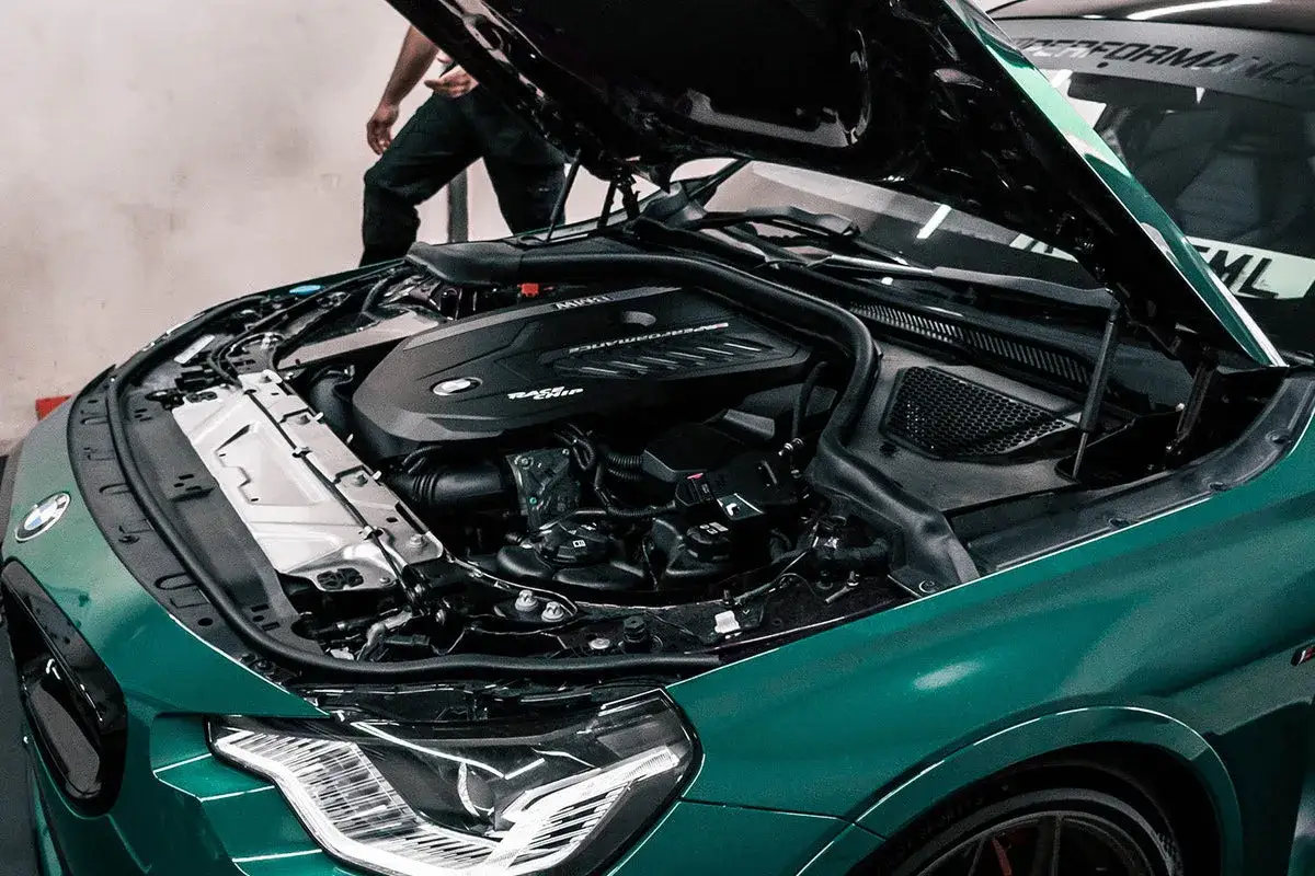 Zielony BMW z otwartą maską, odsłaniający silnik b58. Mechanik w tle.