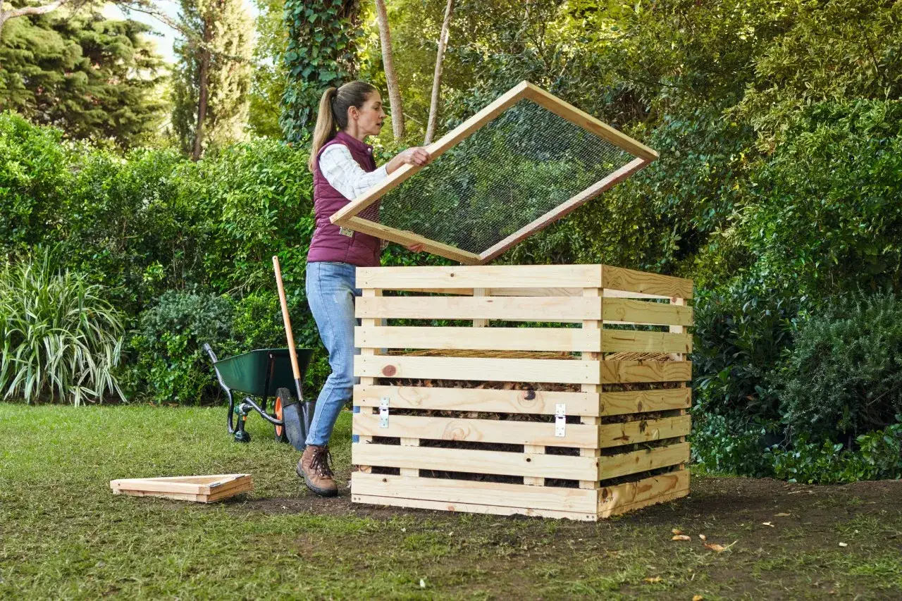 Frau baut einen Kompost, hält ein Sieb über die Holzkiste.