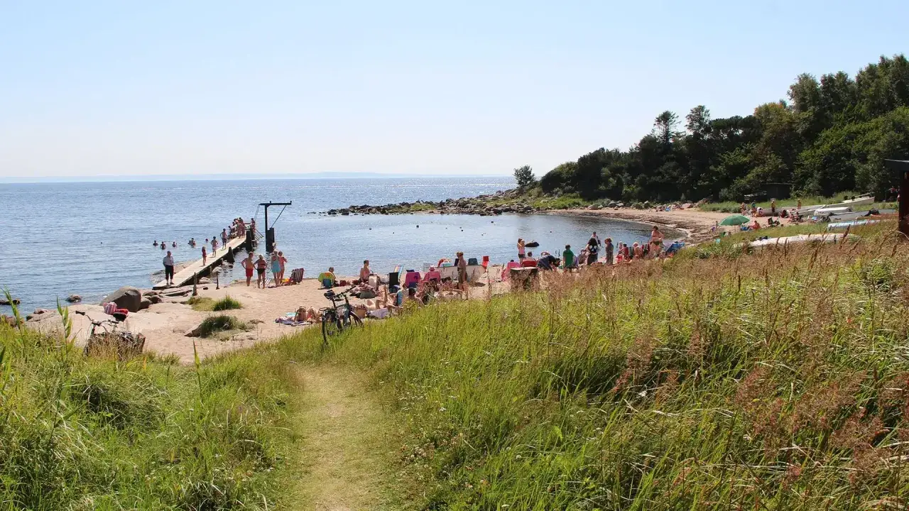 Solig stranddag med badgäster vid en brygga och på sanden. Många njuter av sommarvärmen, perfekta aktiviteter Halmstad.