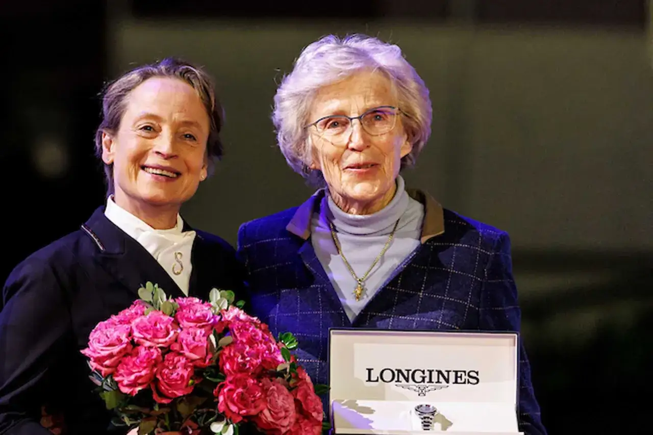 Zwei Frauen, eine mit Blumenstrau&szlig;, die andere mit einer Longines-Box, stehen nebeneinander. Madeleine Winter Schulze l&auml;chelt.