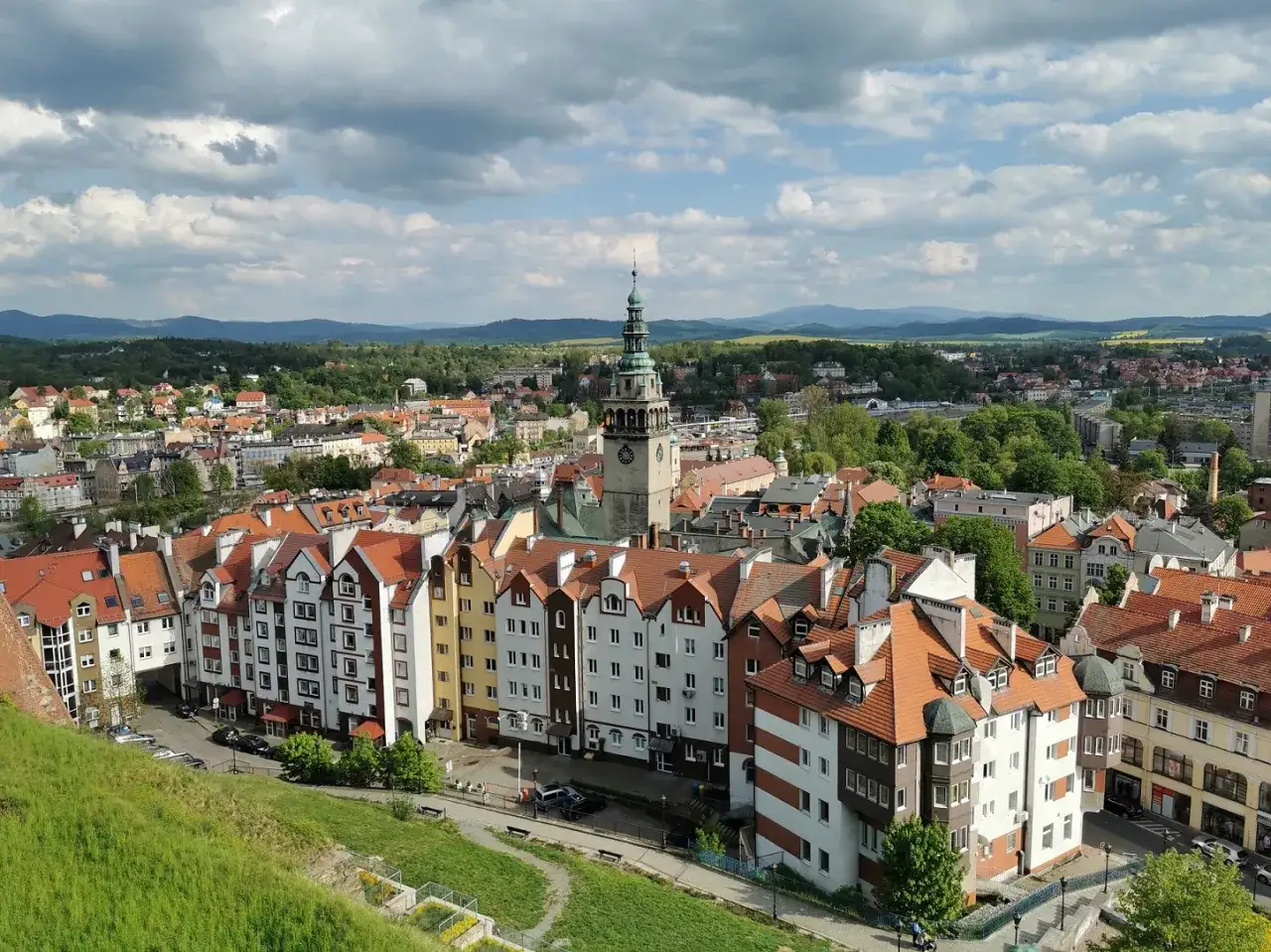 Widok na kłodzko stare miasto z wieżą ratuszową i kolorowymi kamienicami. W tle zielone wzg&oacute;rza.