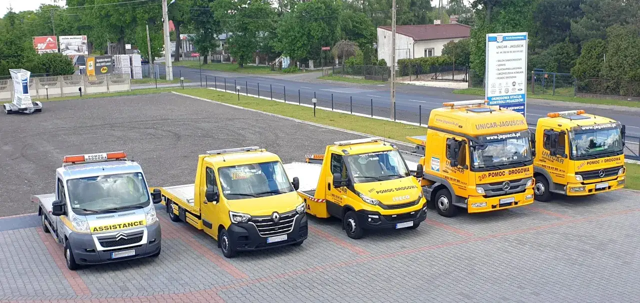 Flota pojazdów pomocy drogowej, w tym jeden z napisem ASSISTANCE, gotowa do akcji.