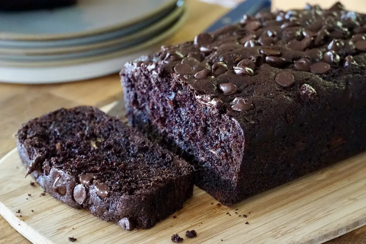 Saftiger zucchini schoko kuchen mit Schokost&uuml;ckchen, frisch gebacken und auf einem Holzbrett angerichtet.