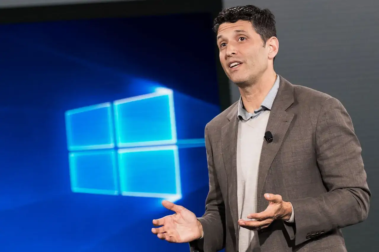 Mężczyzna w garniturze prezentuje logo Windows 9 na niebieskim tle.