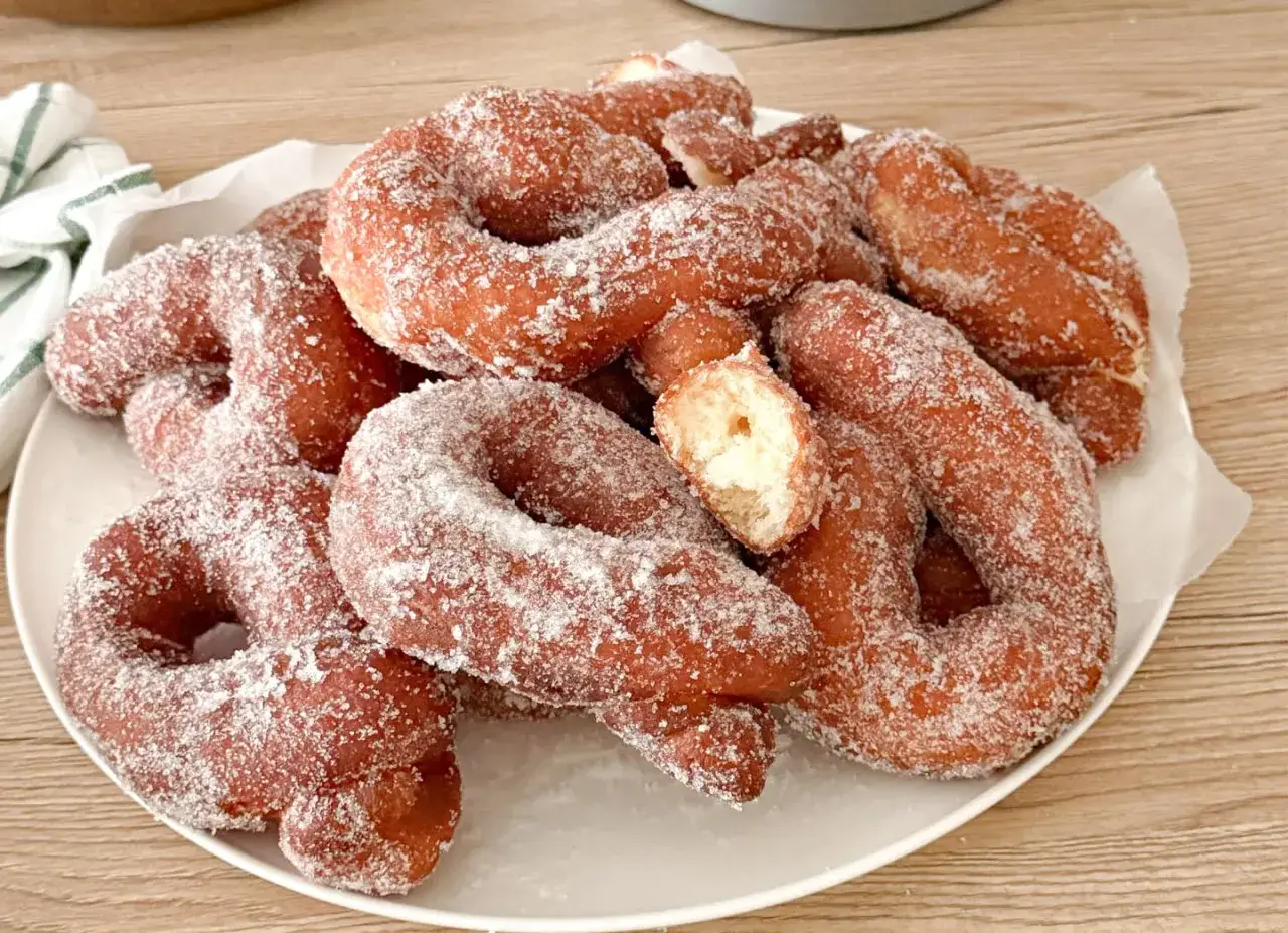 Un piatto colmo di zeppole fritte napoletane, dorate e cosparse di zucchero. Una delizia da gustare!