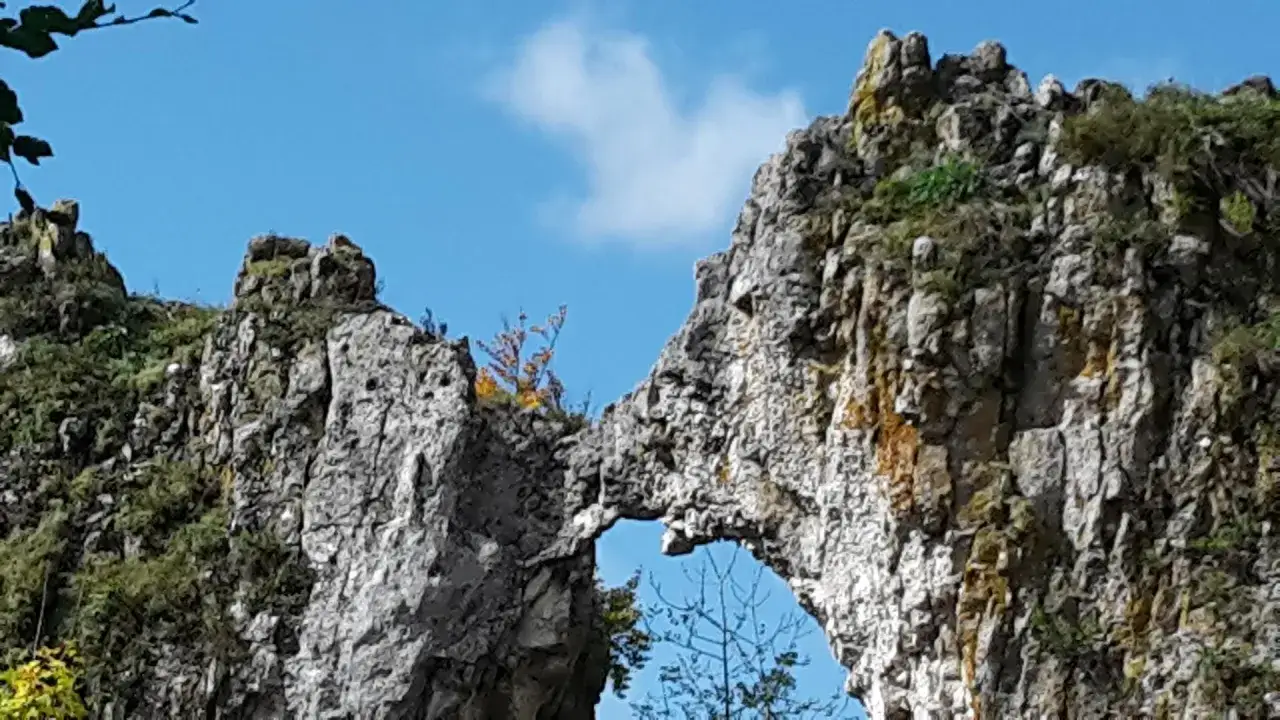 Felsenlabyrinth Blaubeuren: Ein nat&uuml;rliches Felsentor mit zerkl&uuml;fteten Felsen und gr&uuml;ner Vegetation unter blauem Himmel.