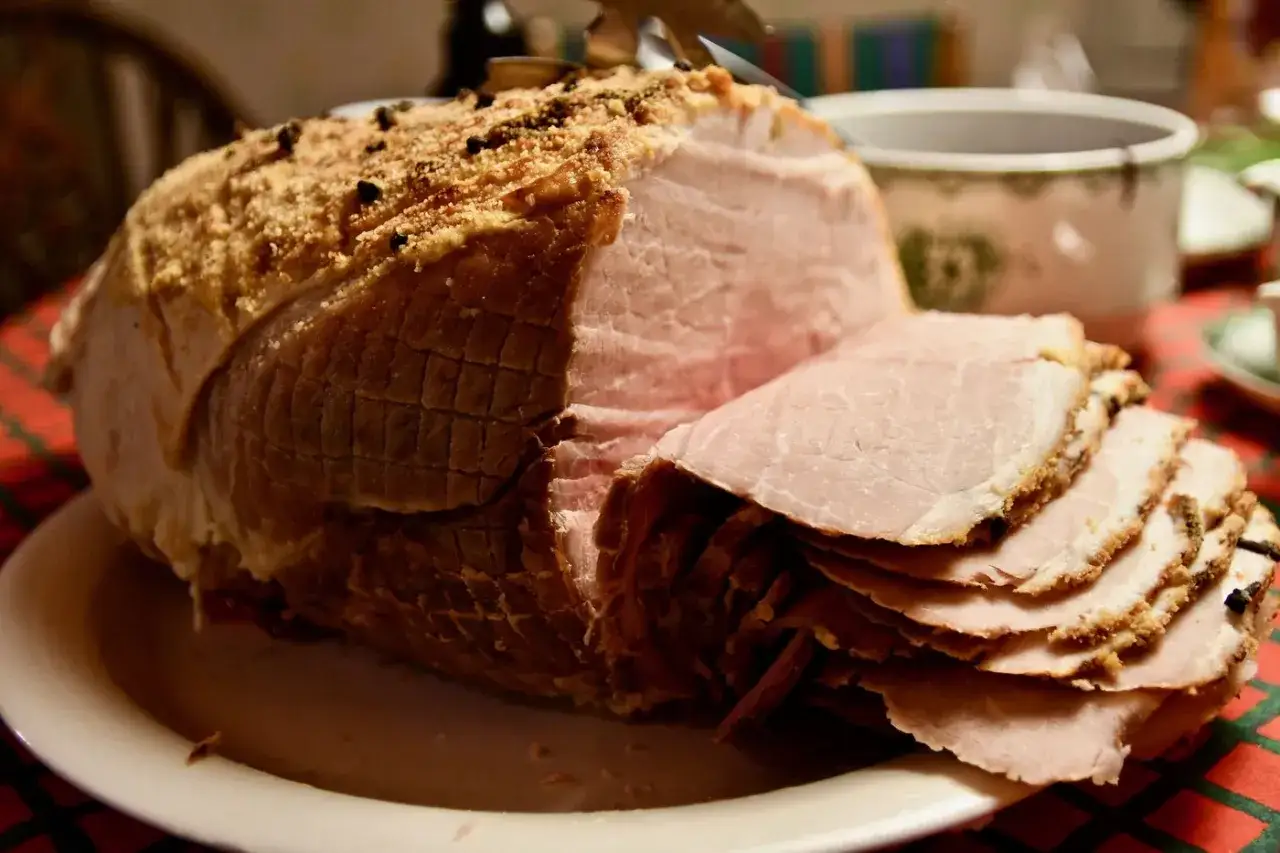 En saftig julskinka med krispig yta, perfekt för en hund att drömma om. Skivorna ligger staplade, redo att serveras.