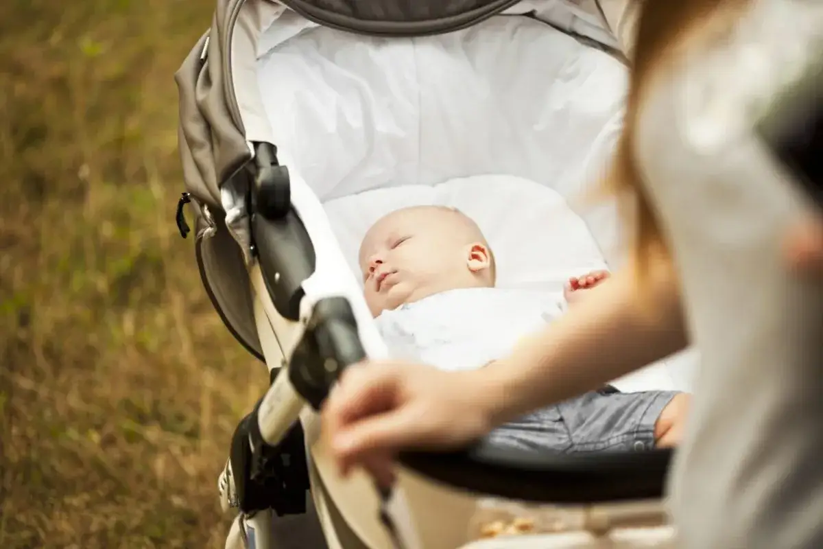 Pierwszy spacer z noworodkiem. Maluch śpi spokojnie w wózku, a mama delikatnie go pcha.