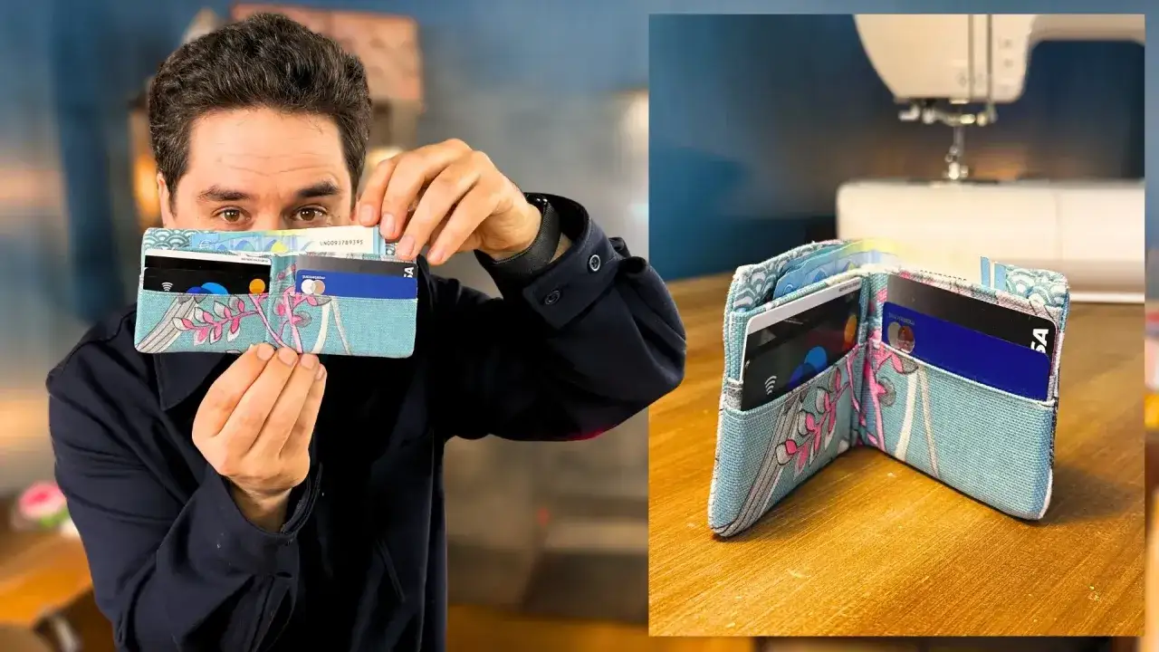 Un homme présente un portefeuille en tissu bleu clair orné de motifs floraux roses. Ce portefeuille, parfait pour un tuto enveloppe rectangulaire, contient des cartes bancaires et des billets.