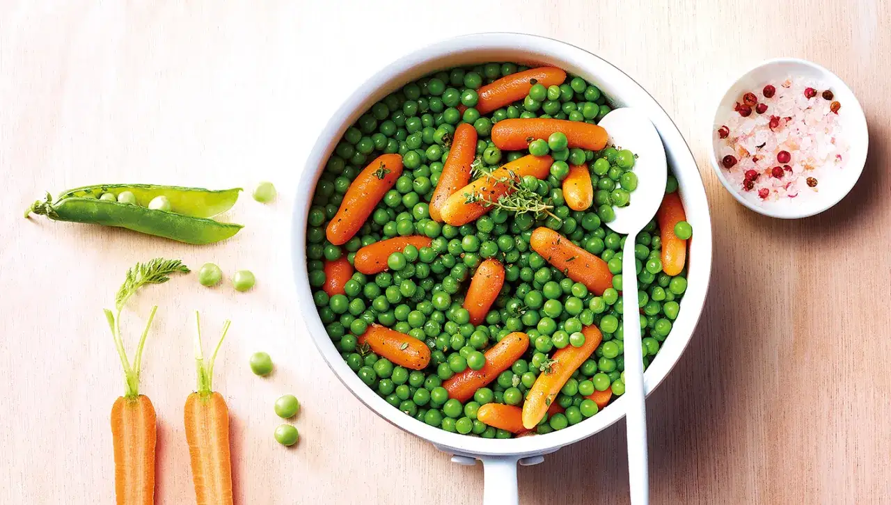 Un plat appétissant de petit pois carotte, garni de thym frais. À côté, des carottes coupées et des cosses de pois.