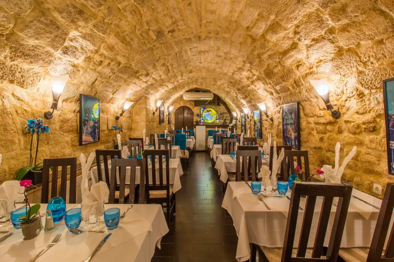 Ambiance de restaurant moyen âge avec murs en pierre, tables dressées et lumières tamisées.