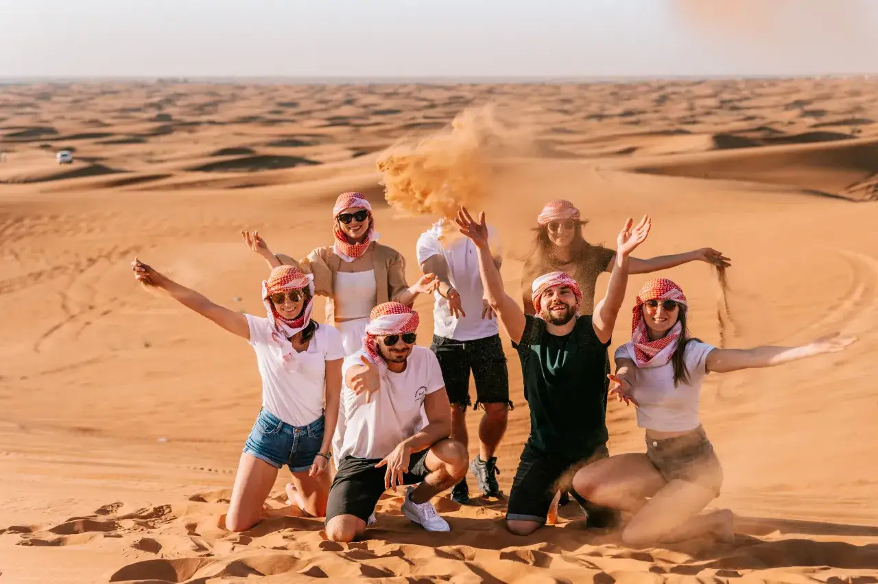 Grupa przyjaci&oacute;ł w pustynnym krajobrazie, gdzie leży Dubaj. Piasek wzbija się w powietrze, tworząc magiczną atmosferę.