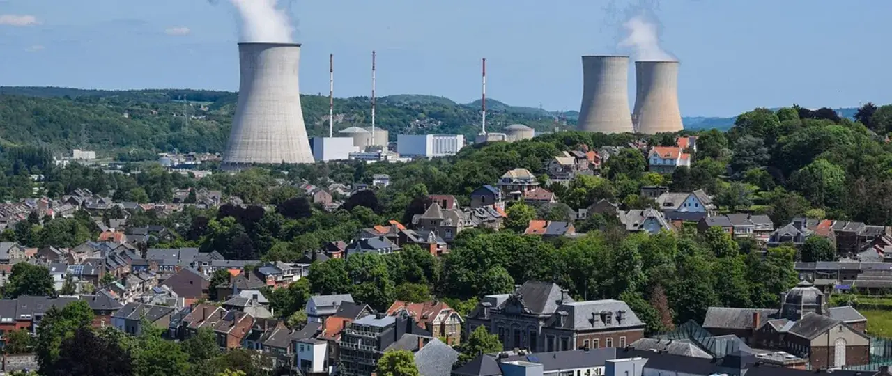 Widok na miasto z elektrownią jądrową w tle. Chmury pary unoszą się z kominów chłodniczych, sugerując pracę instalacji, która może generować promieniowanie jonizujące.