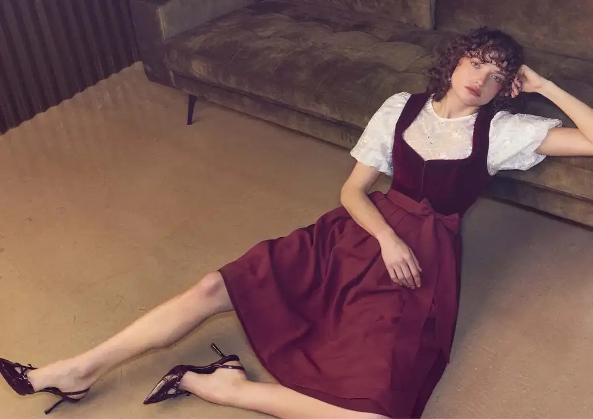Ein Model tr&auml;gt ein elegantes, weinrotes Mini Dirndl extra kurz mit wei&szlig;er Bluse und hohen Schuhen.