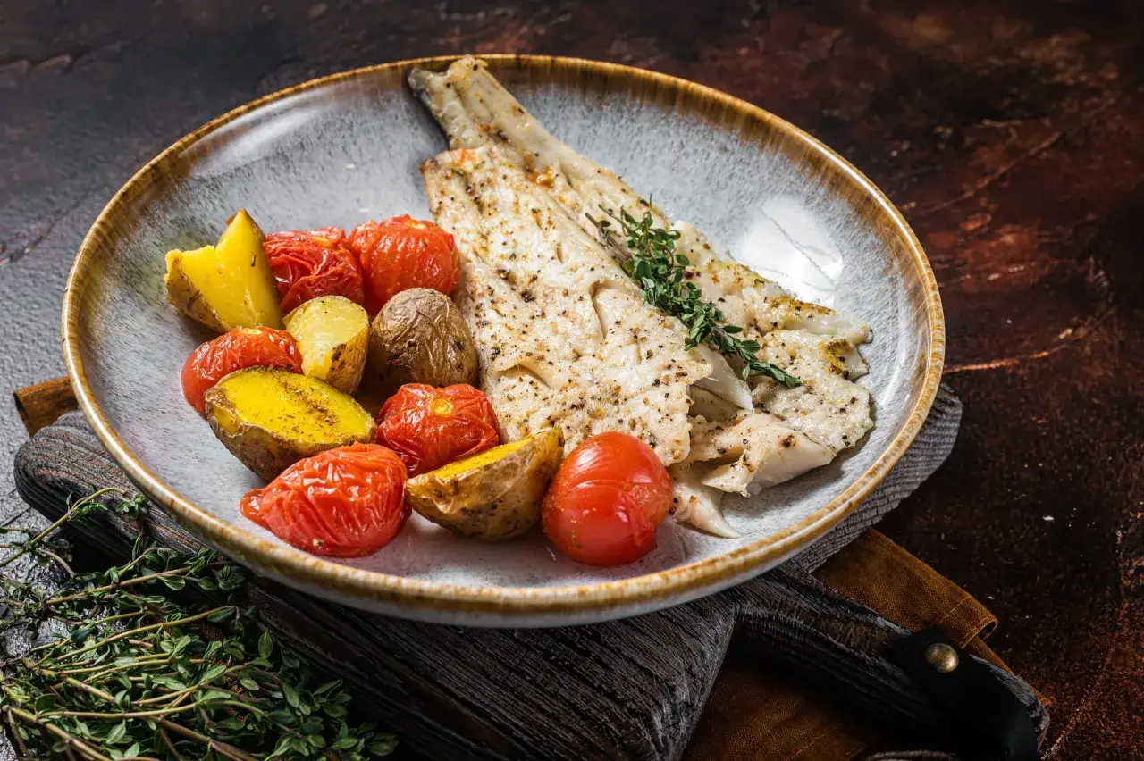 Delicioso abadejo a la plancha con patatas asadas y tomates cherry, adornado con tomillo fresco.