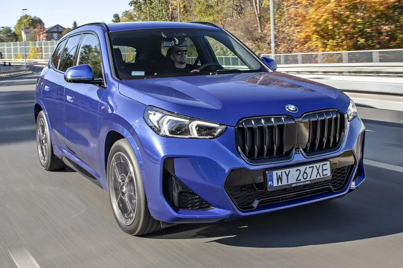 Niebieskie x1 bmw jedzie po drodze, kierowca w okularach przeciwsłonecznych.