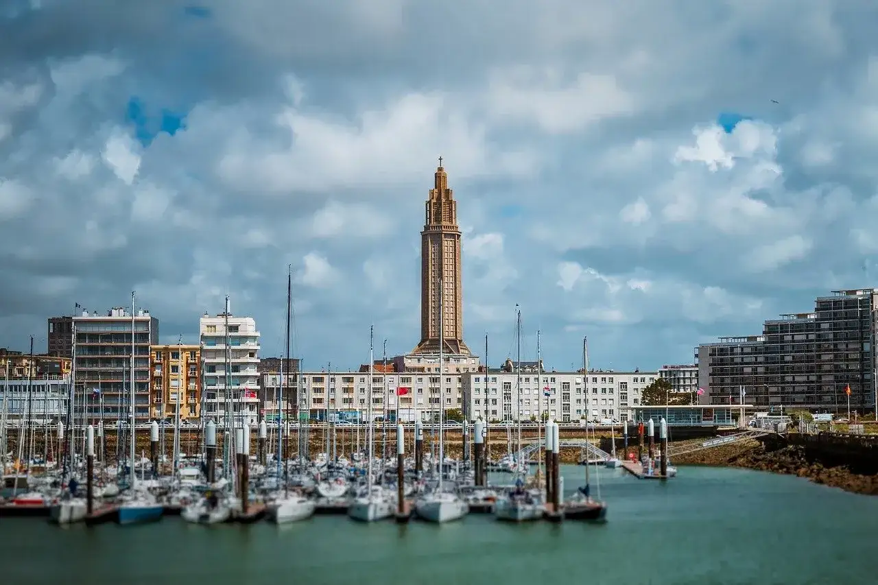 Barche a vela ormeggiate nel porto di Le Havre, con un'imponente torre sullo sfondo e edifici moderni.