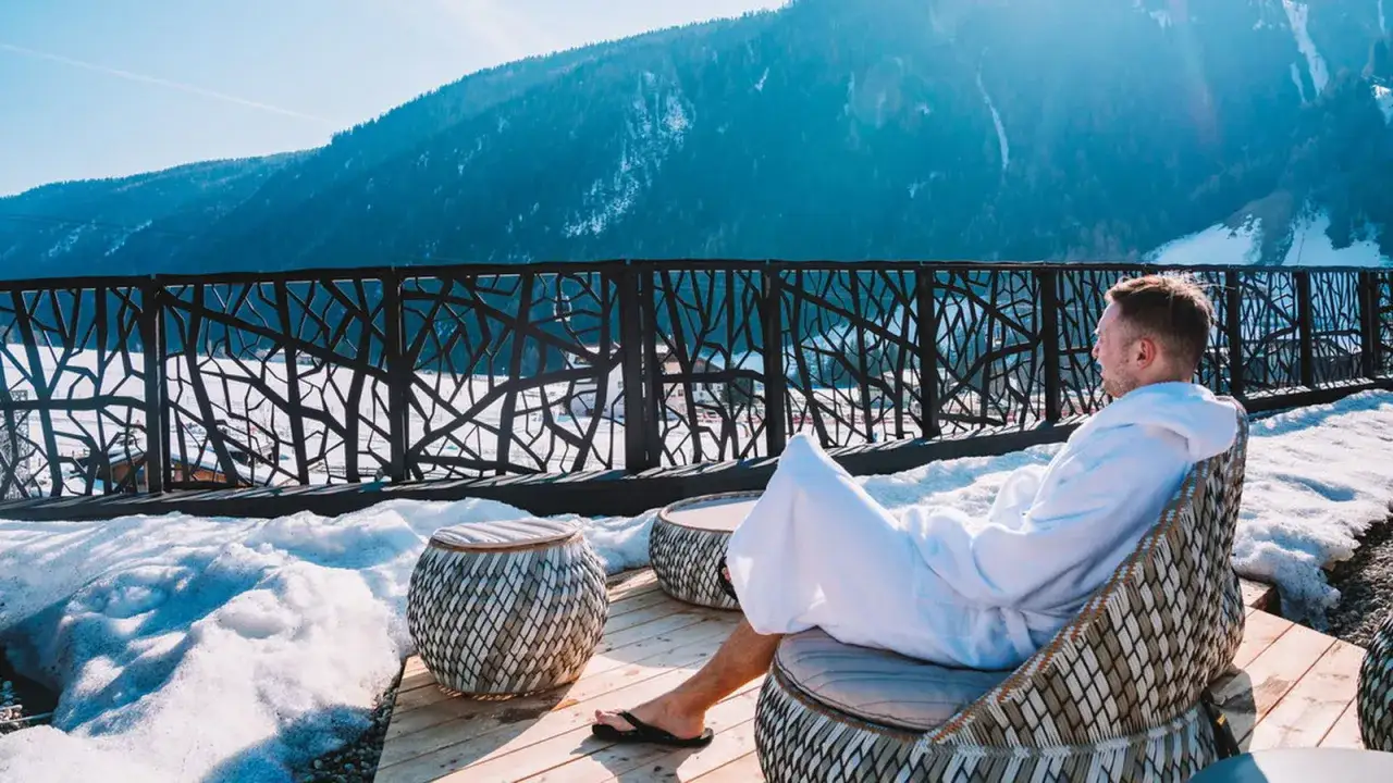 Mann im Bademantel genie&szlig;t die Aussicht auf verschneite Berge. Ein entspannter Badeurlaub in Bayern, auch im Winter ein Genuss.