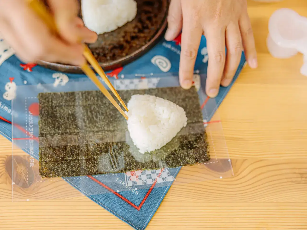 Hands use chopsticks to place a rice ball on nori. Wondering if you can freeze onigiri? This image shows the start of making them.