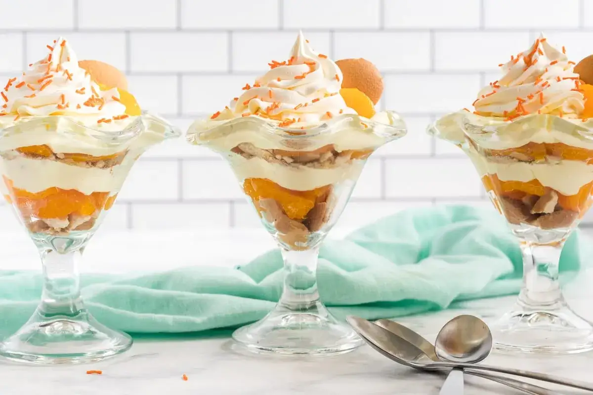 Drei k&ouml;stliche Desserts im Glas mit Pfirsichschichten, Keksen und Sahne, garniert mit orangen Streuseln und Keksen.
