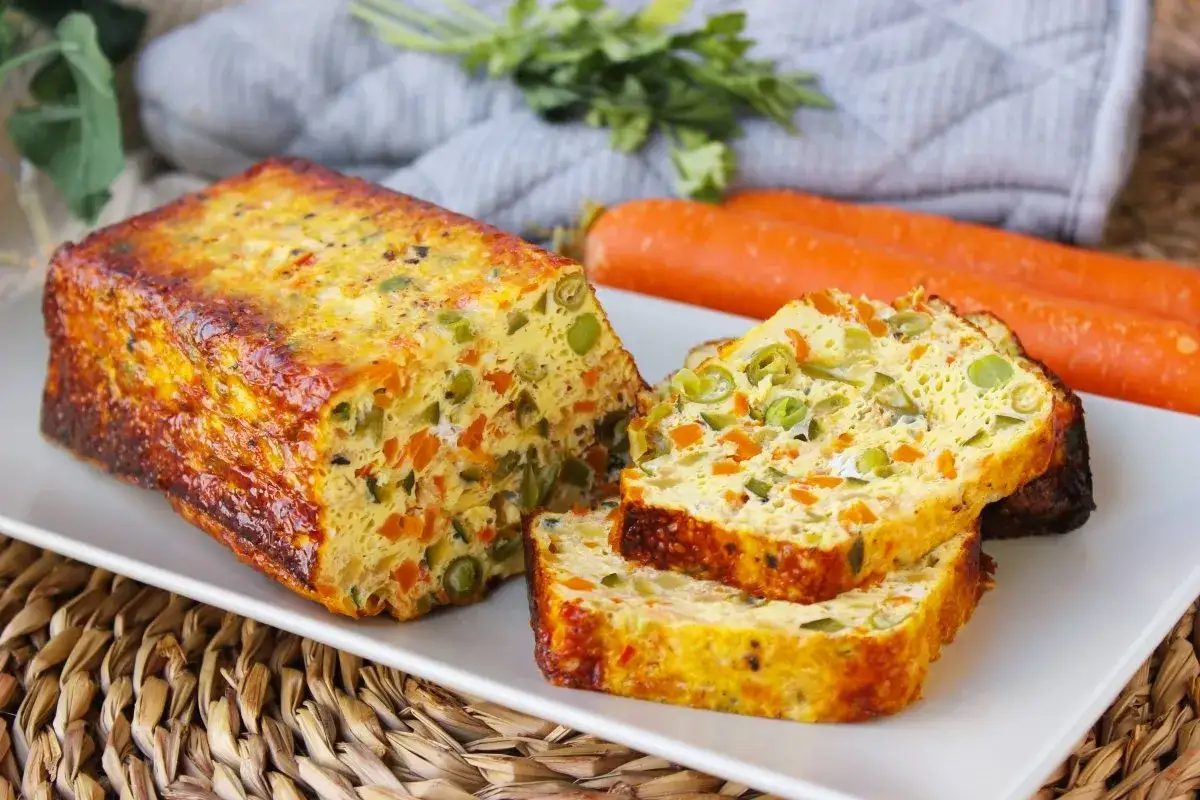 Pastel de verduras al horno, con trozos de zanahoria y guisantes, servido en una bandeja blanca.