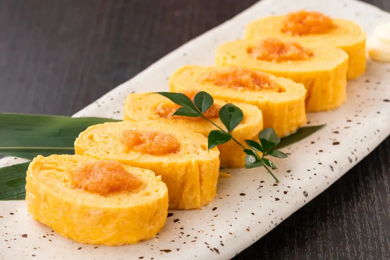 Rouleaux d'oeuf japonais, dorés et moelleux, garnis d'une touche orangée, présentés sur une assiette décorative avec une feuille verte.