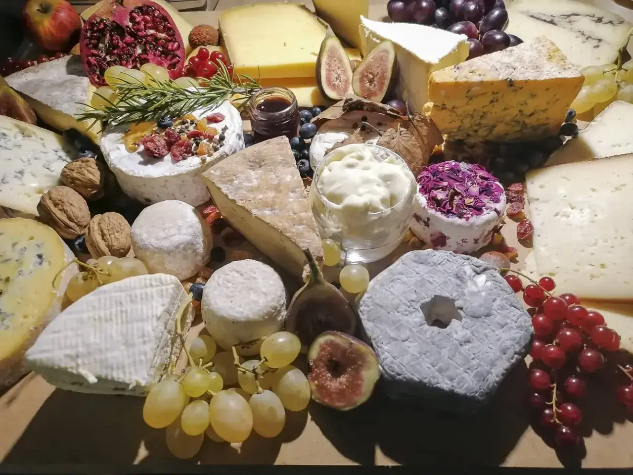 Plateau de fromages variés, dont un fromage à croûte lavée grisâtre, fruits, noix et confiture.