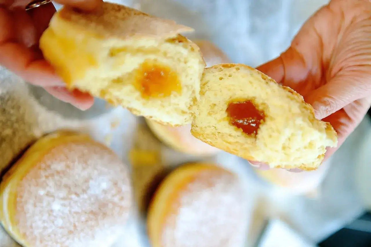 Ein Krapfen wird auseinandergebrochen, das Innere mit Marmelade ist sichtbar. Ein köstliches Krapfen Rezept zum Nachbacken.