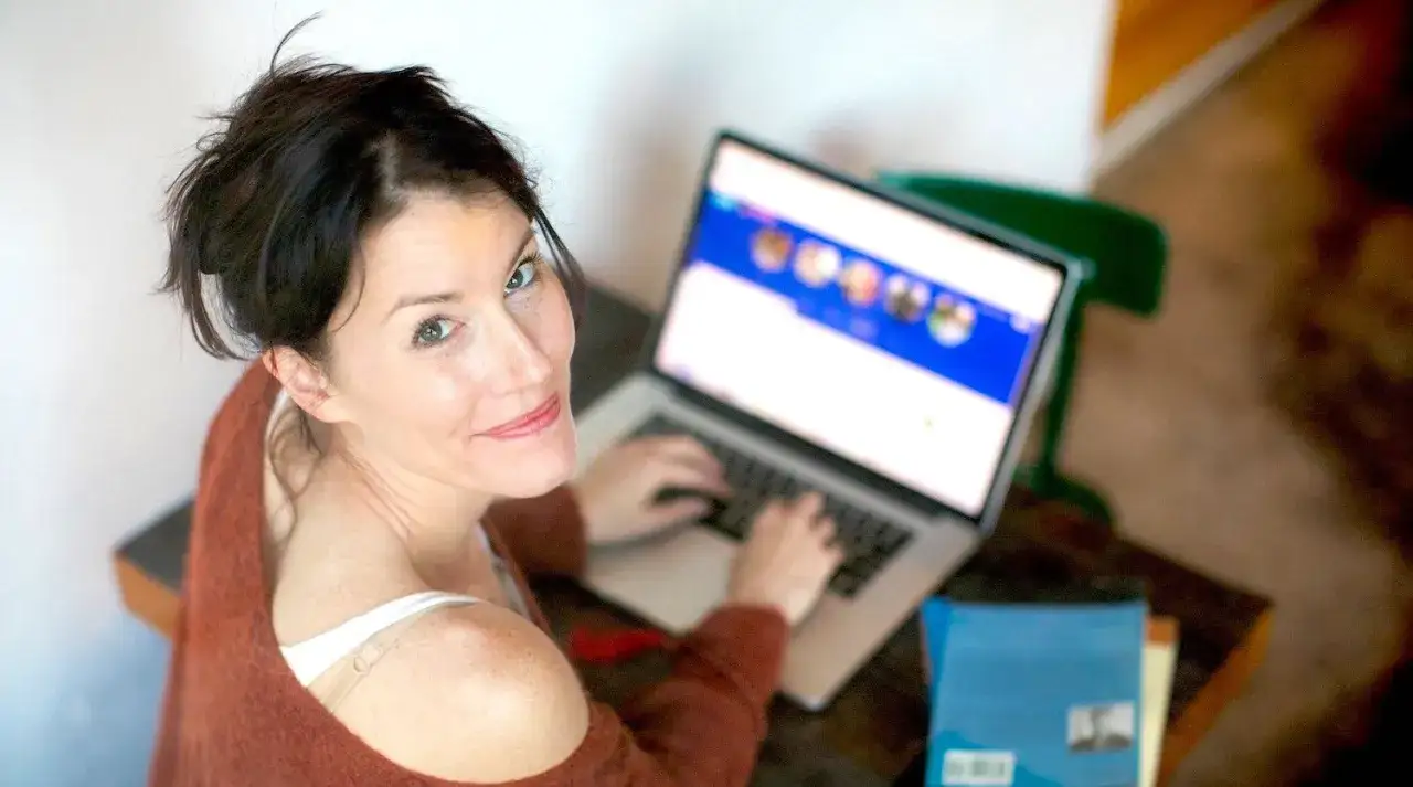 Donna sorride mentre digita al computer, forse sta seguendo un **inglese corso gratis** per migliorare le sue competenze.