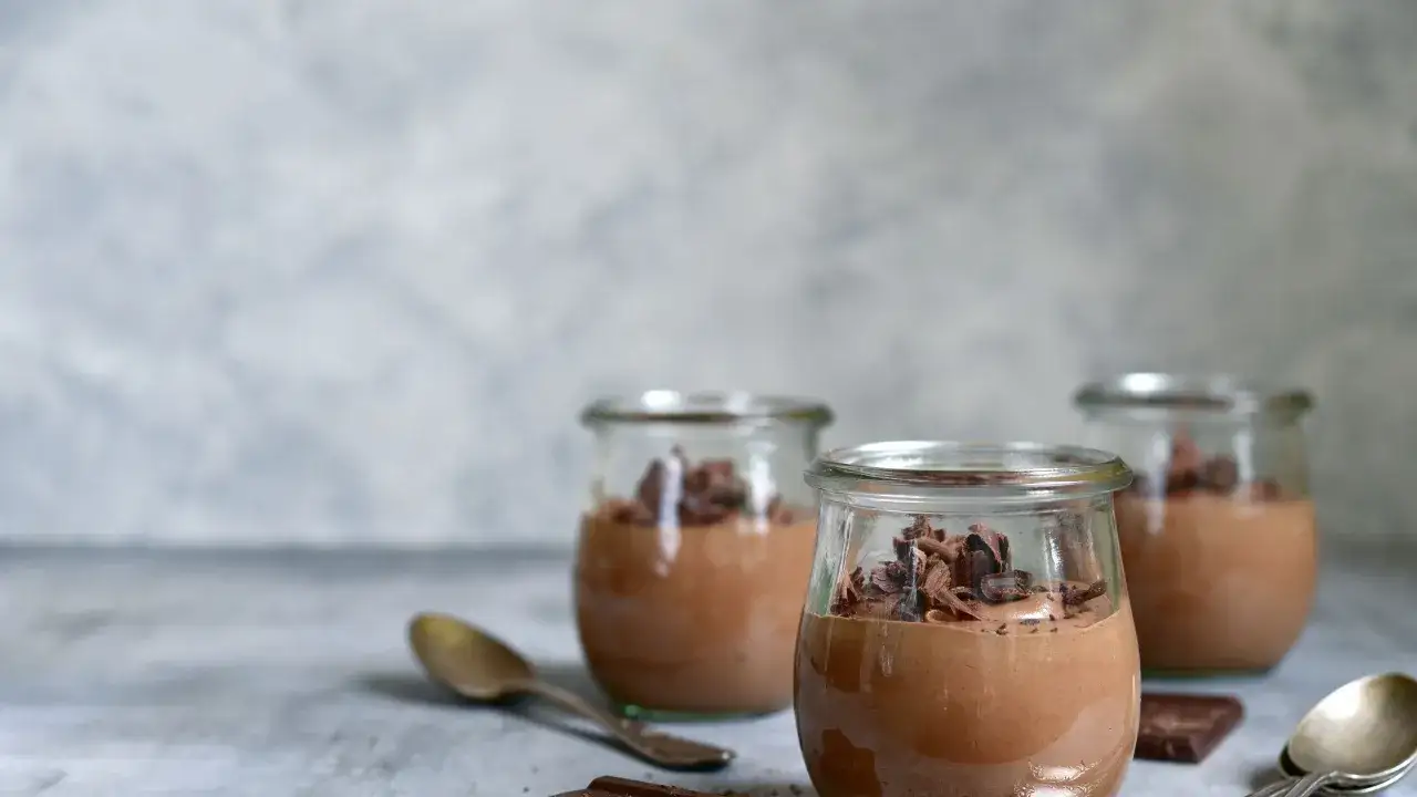 Tre vasetti di budino fatto in casa al cioccolato, guarniti con riccioli di cioccolato fondente.