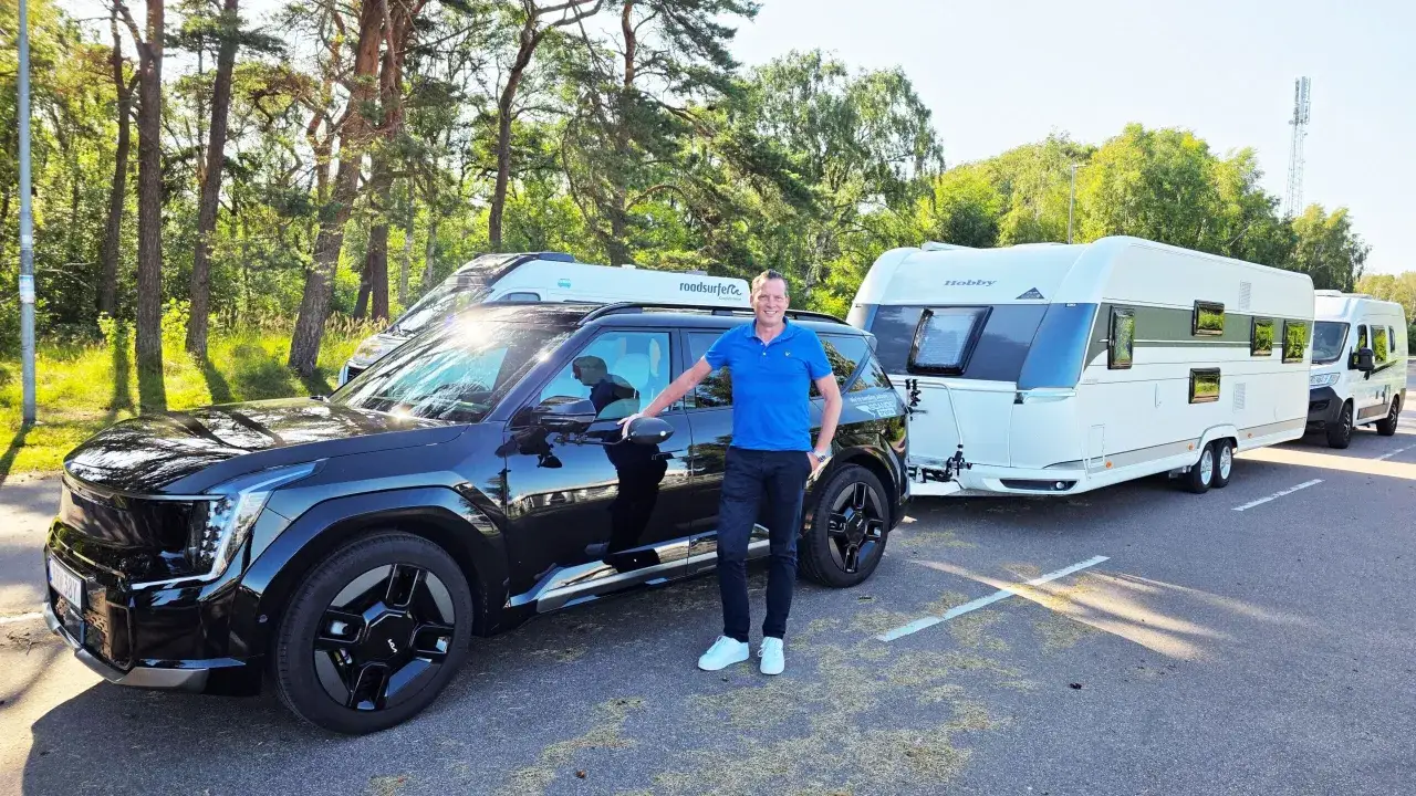 Man vid en svart elbil som drar en husvagn och en campervan. Perfekt för sommarens äventyr!