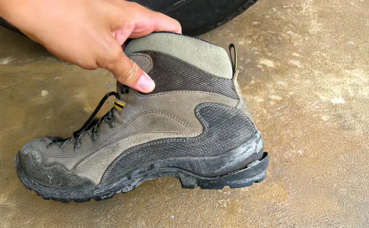 A hand holds a worn hiking boot with a cracked sole, showing why shoe soles crack due to age and wear.