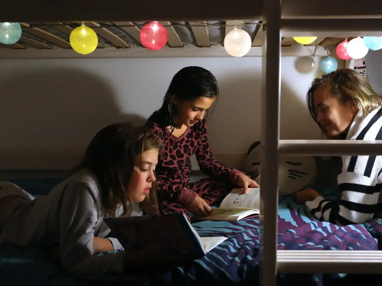 Padre lee cuentos para ni&ntilde;os de 7 a&ntilde;os en una litera iluminada por luces de colores.