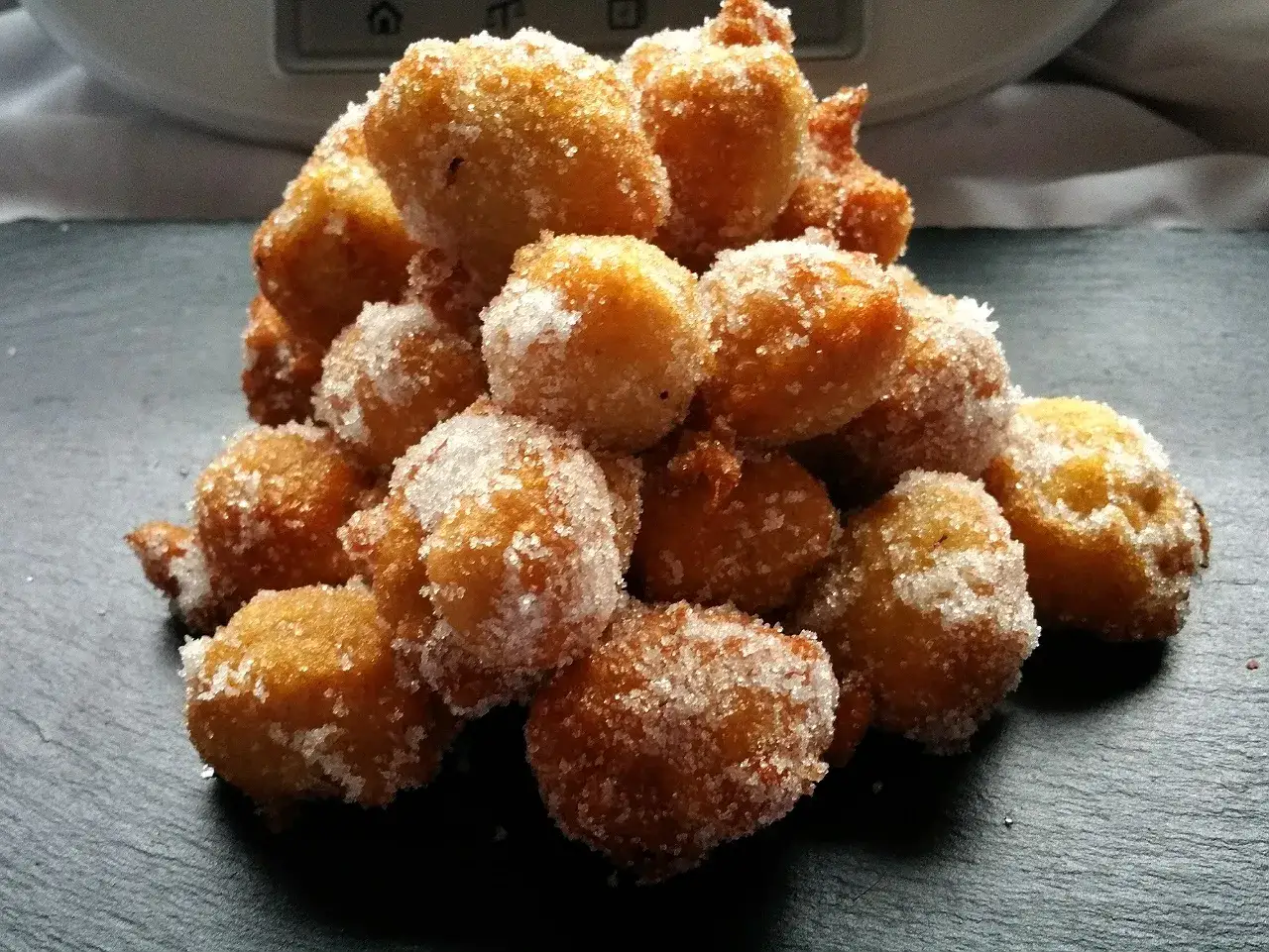Montón de buñuelos de viento dorados y crujientes, espolvoreados con azúcar.