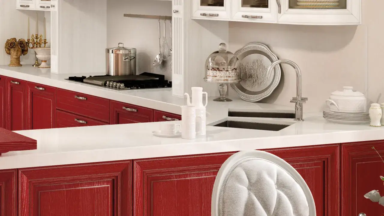 Cucina con ante rosse, piano bianco, pentola sul fornello, torta sotto campana di vetro. Okite cos'è? Un piano di lavoro resistente e bello.