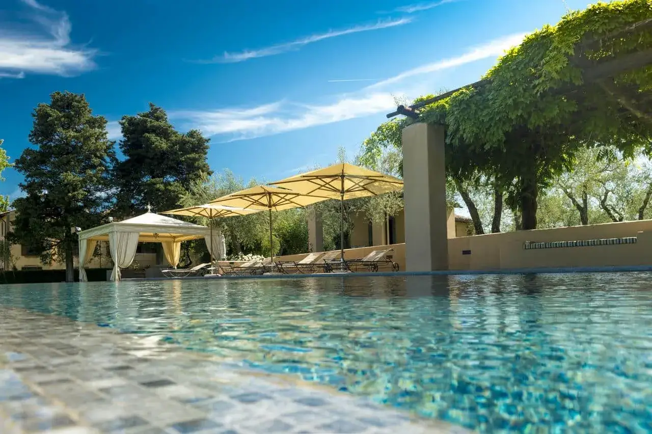 Piscina con lettini e ombrelloni, ideale per un weekend fuori porta Roma. Cielo azzurro e vegetazione rigogliosa.