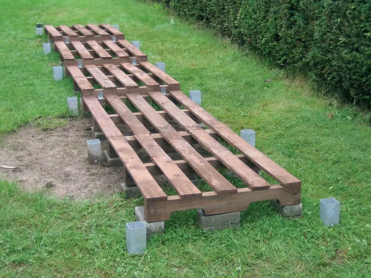 Holzpaletten auf Betonsteinen und Metallpfosten f&uuml;r den brennholz lagern untergrund. So bleibt das Holz trocken.
