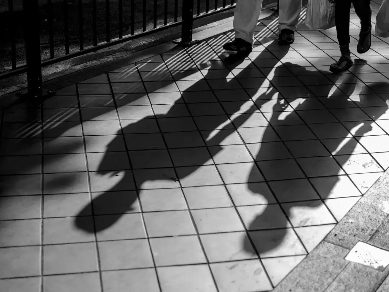 Sombras alargadas de personas caminando sobre baldosas, creando **fotos creativas** con un juego de luces y líneas.