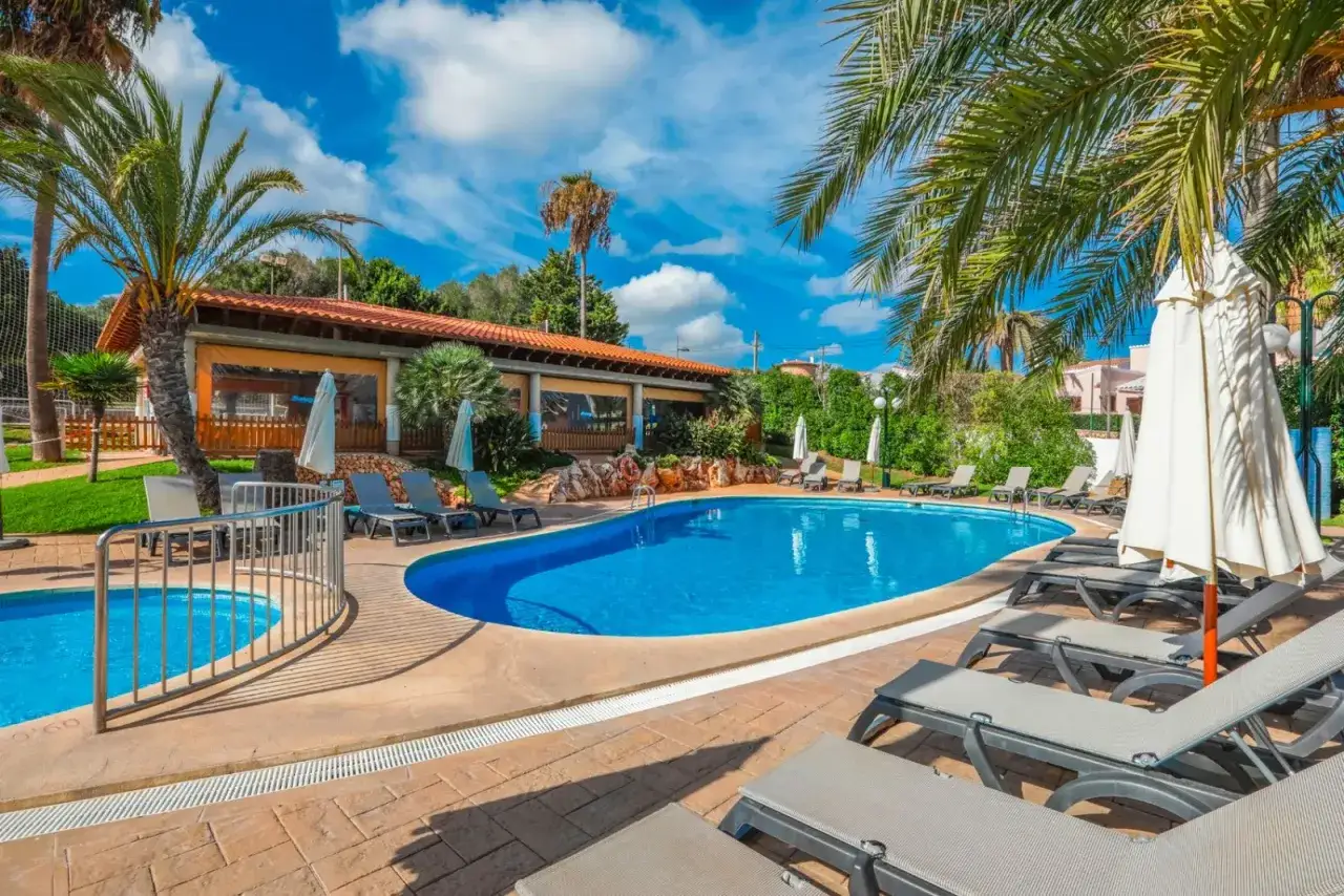 Piscina azzurra e lettini prendisole al **hotel Occidental Menorca**, con palme e cielo azzurro.