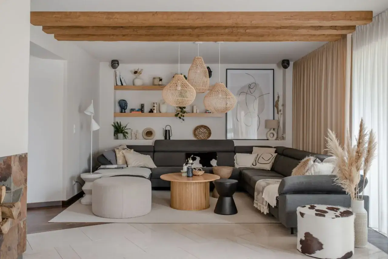 Przytulny salon w stylu boho z szarą sofą, plecionymi lampami i drewnianymi belkami na suficie.
