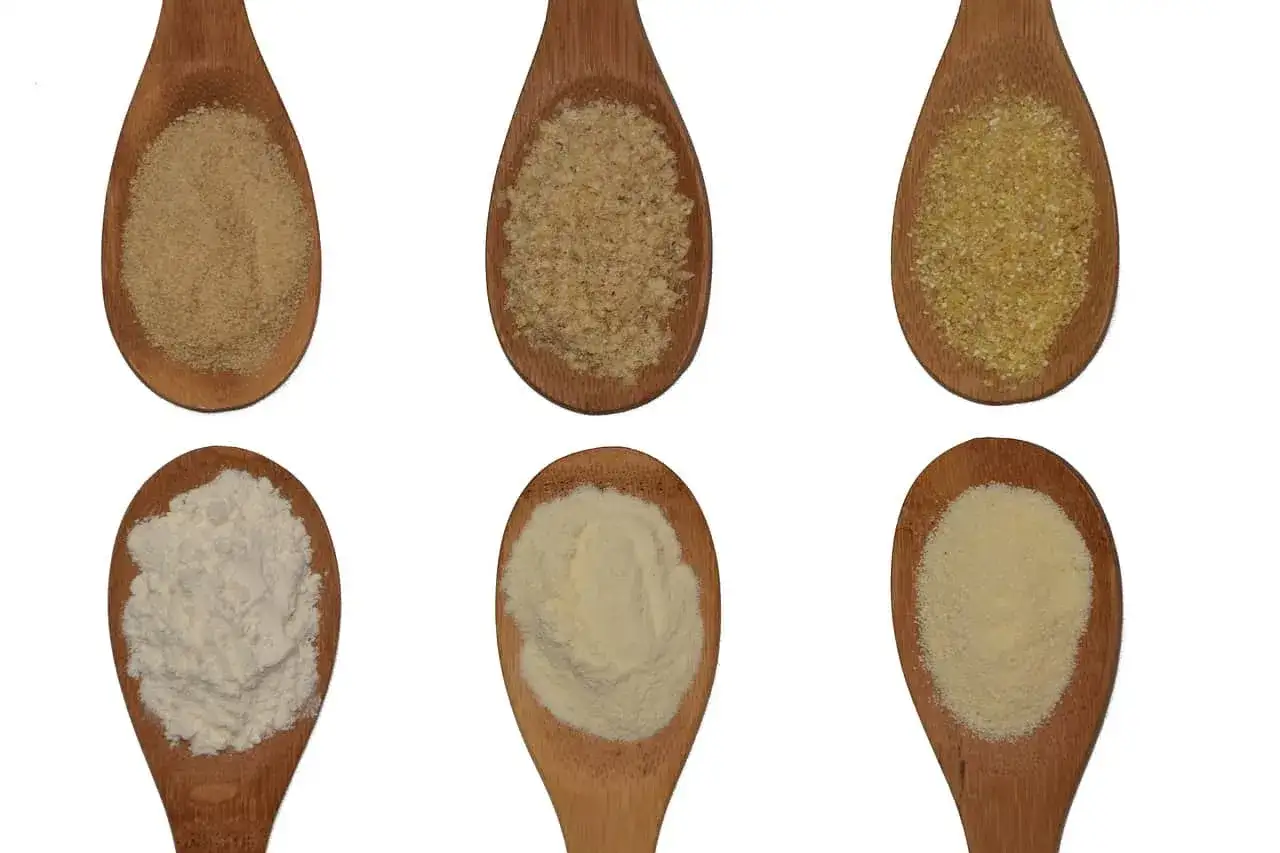 Sei cucchiai di legno mostrano diverse granulosit&agrave; di cereali, illustrando la differenza tra semola e semolato.