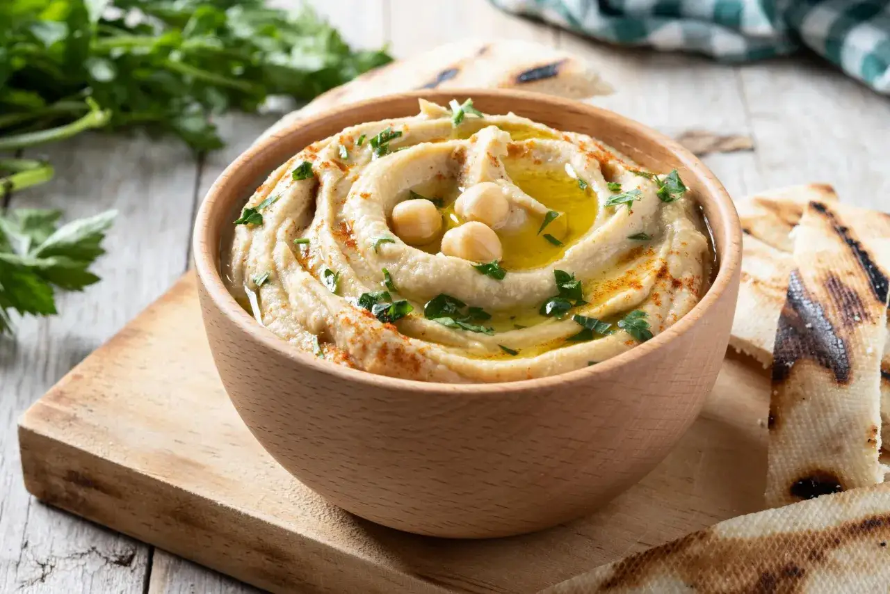 Pyszny hummus z ciecierzycy, polany oliwą, posypany papryką i natką pietruszki, podany z grillowanym pitą.
