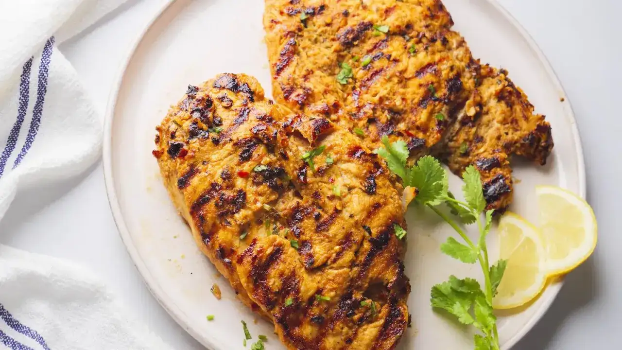 Zwei saftige H&auml;hnchenbrustfilets, perfekt gegrillt mit markanten Streifen. Das Peri Peri Chicken ist mit Kr&auml;utern und Zitronenspalten garniert.